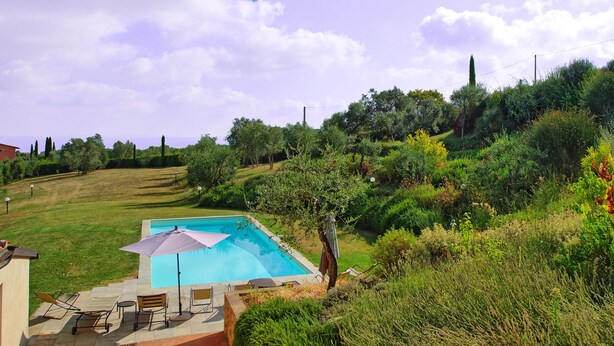 A swimming pool with a patio area, surrounded by lush greenery and hills.