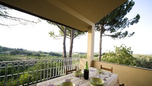 A balcony with a table set for dining, overlooking a scenic landscape with trees and hills.