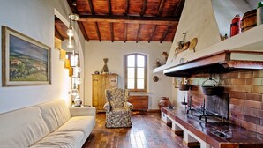 A cozy living room with a wooden ceiling, a white sofa, a floral armchair, and a brick fireplace.