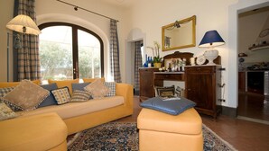 Un salón con un sofá amarillo, un mueble de madera y un comedor con una cocina al fondo.