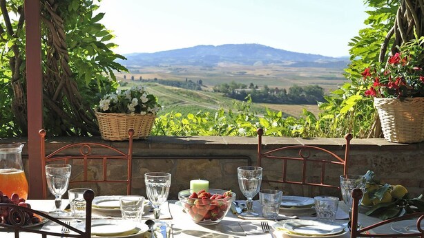 Una mesa dispuesta para una comida con vistas a colinas ondulantes y una cadena montañosa distante.