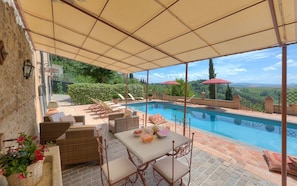 A covered outdoor area with a pool, wicker furniture, and a table with food and drinks.