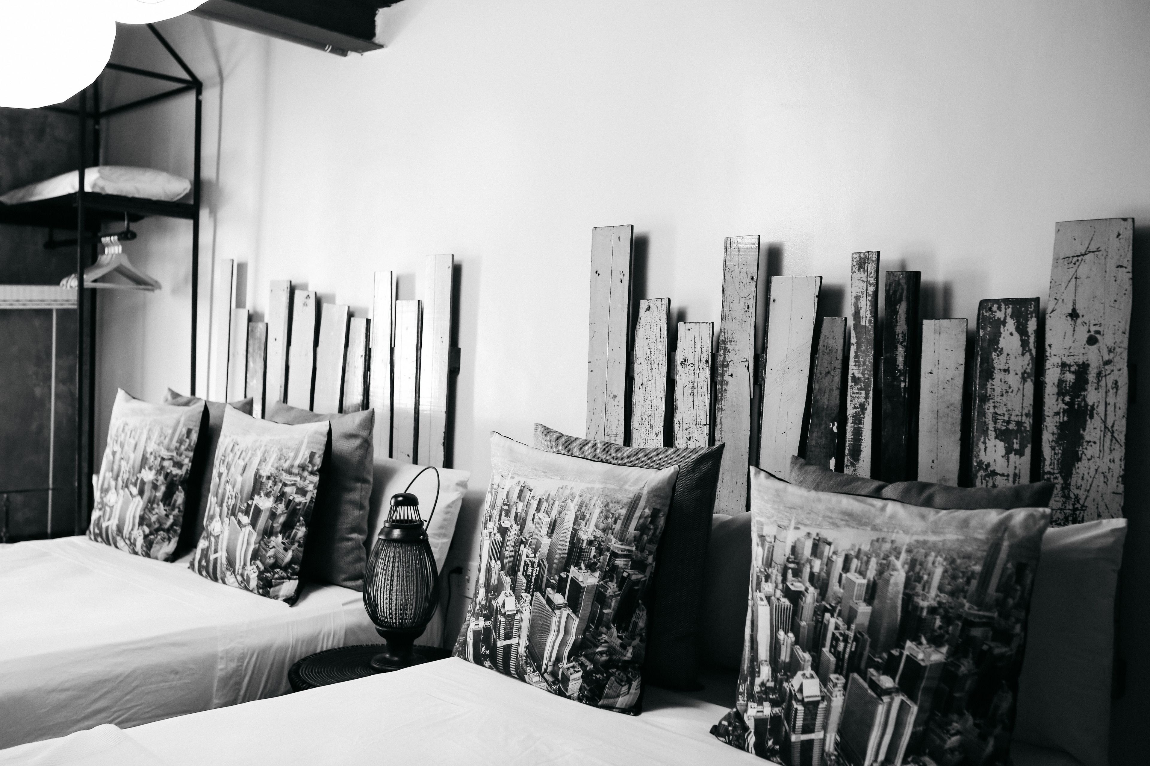 A bedroom with two beds, a cityscape pillow, a lamp, and a wooden headboard.