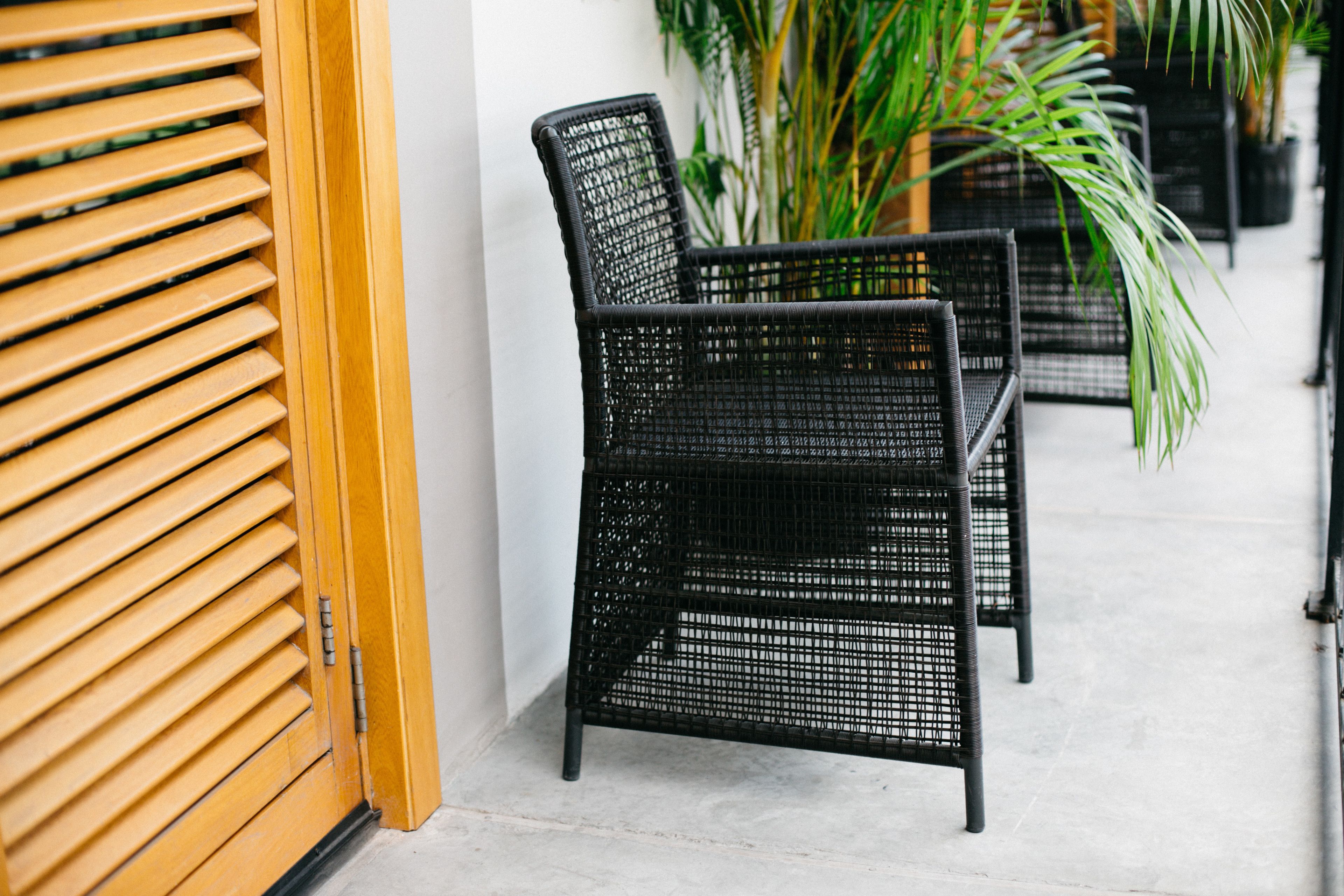 A row of black wicker chairs with a wooden slatted door in the background.