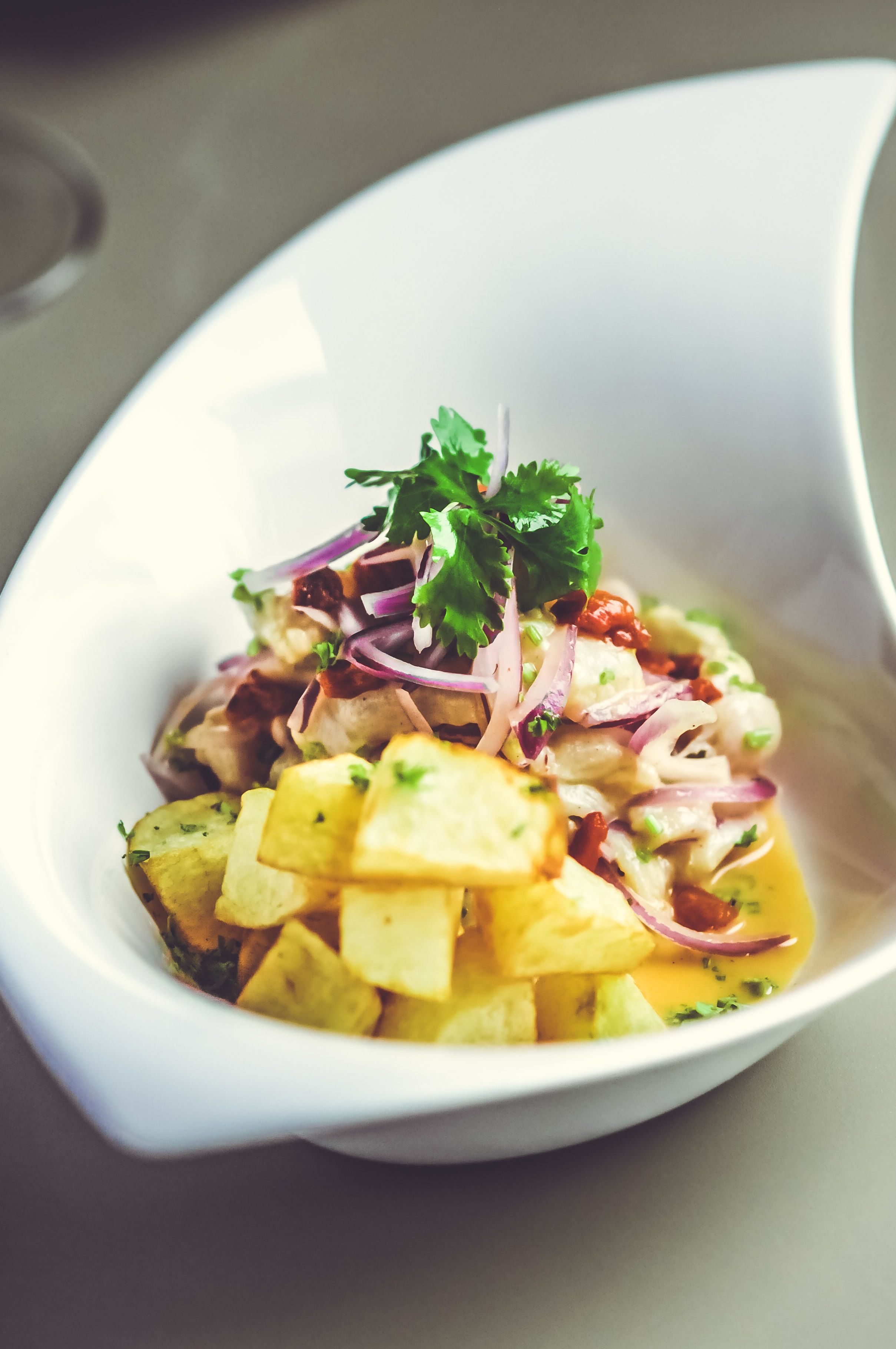 A white bowl containing a dish with diced potatoes, onions, and herbs.