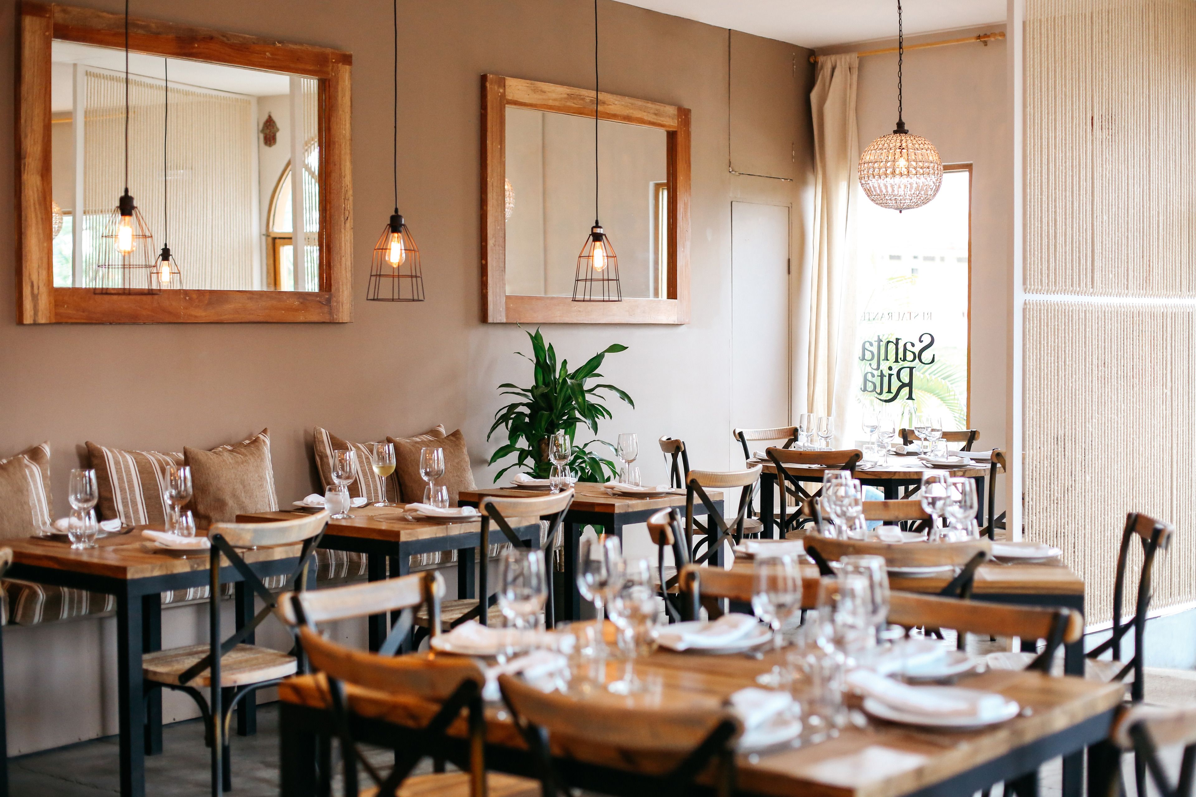 A restaurant with wooden tables and chairs, hanging light fixtures, and large mirrors on the walls.