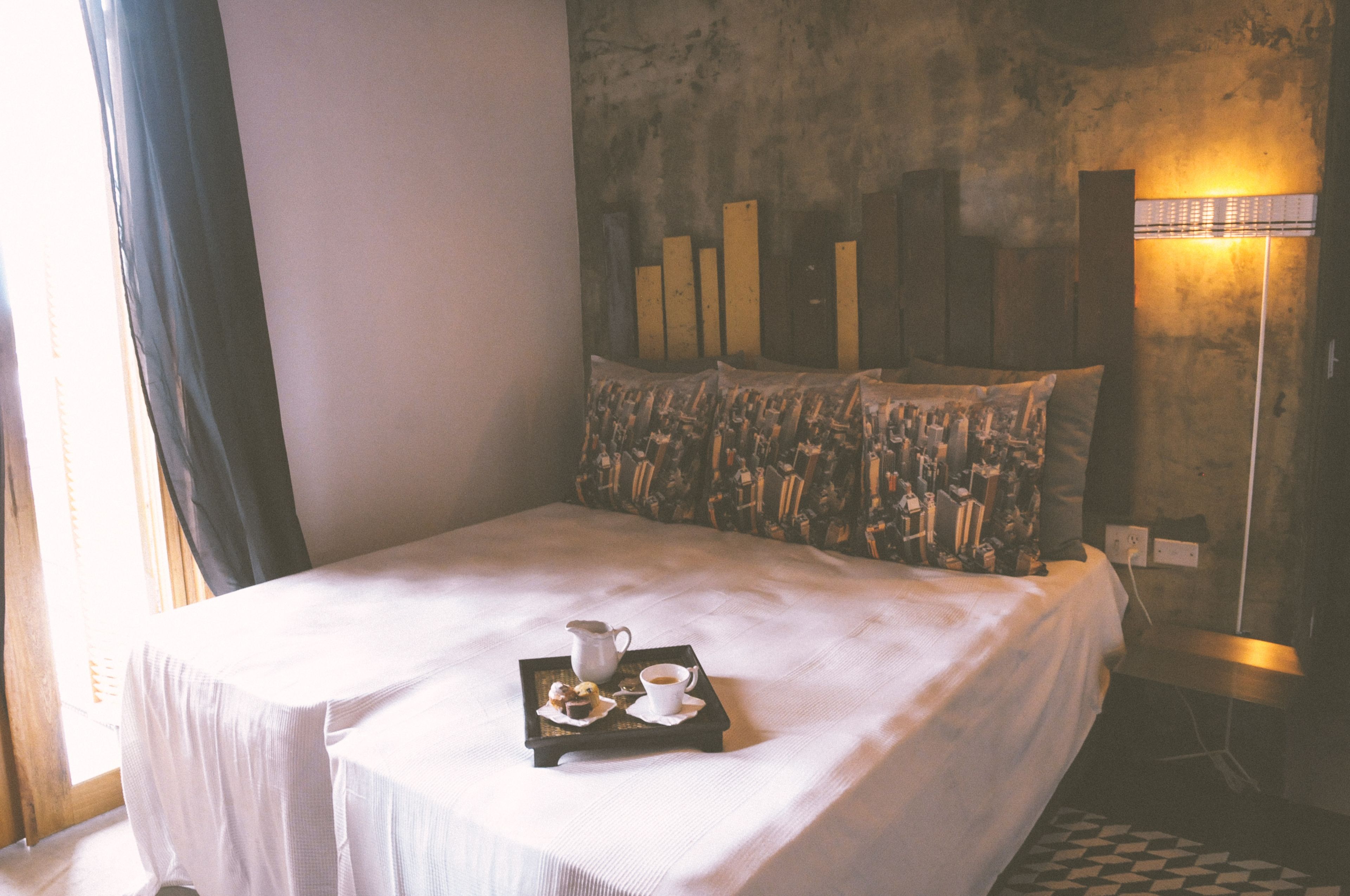 A neatly made bed with a tray of breakfast items, a patterned pillow, and a textured wall.