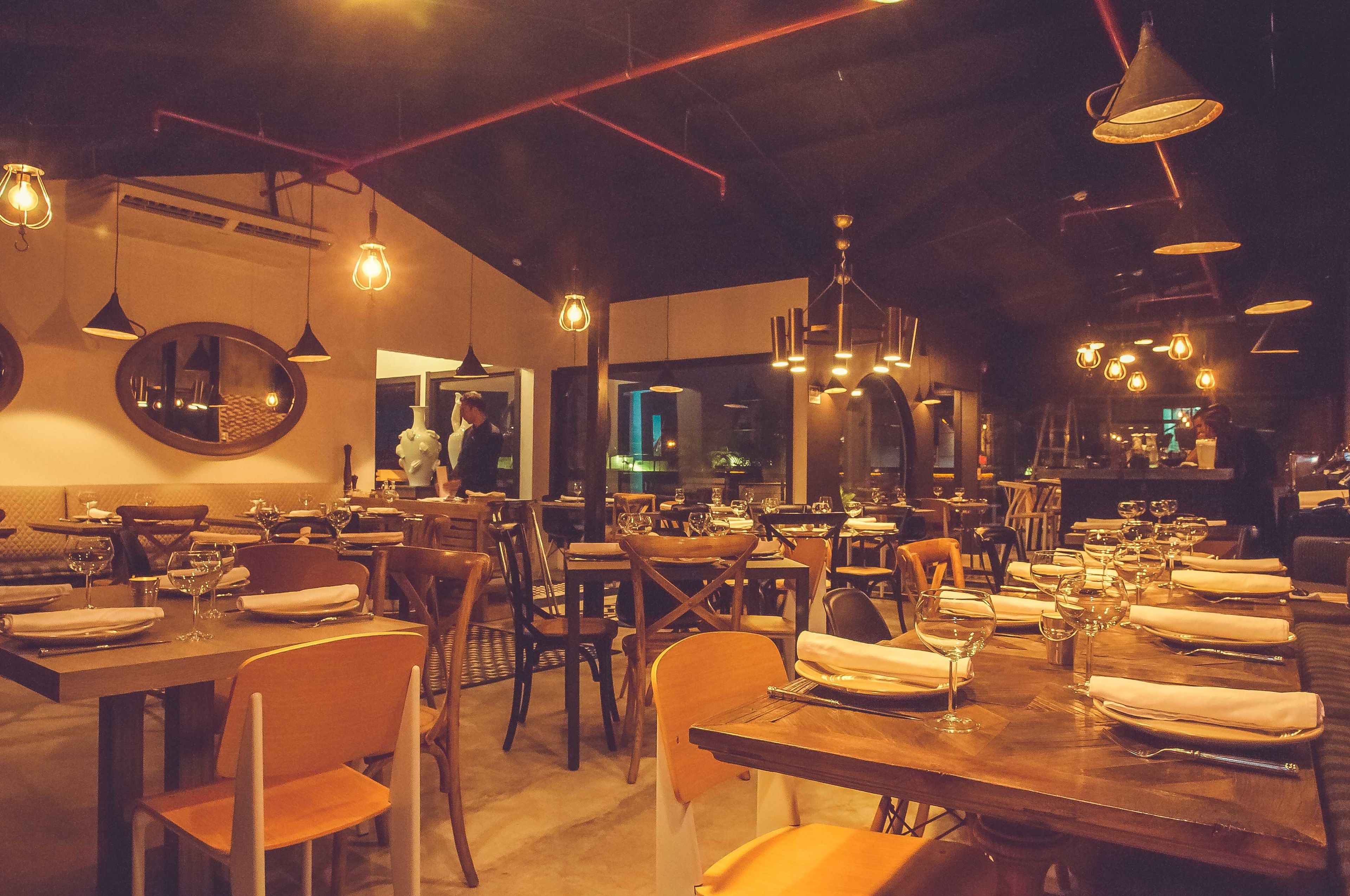 A restaurant with multiple dining tables, chairs, and hanging pendant lights.