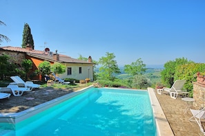 Piscina com espreguiçadeiras, um prédio de pedra e vista para o campo.
