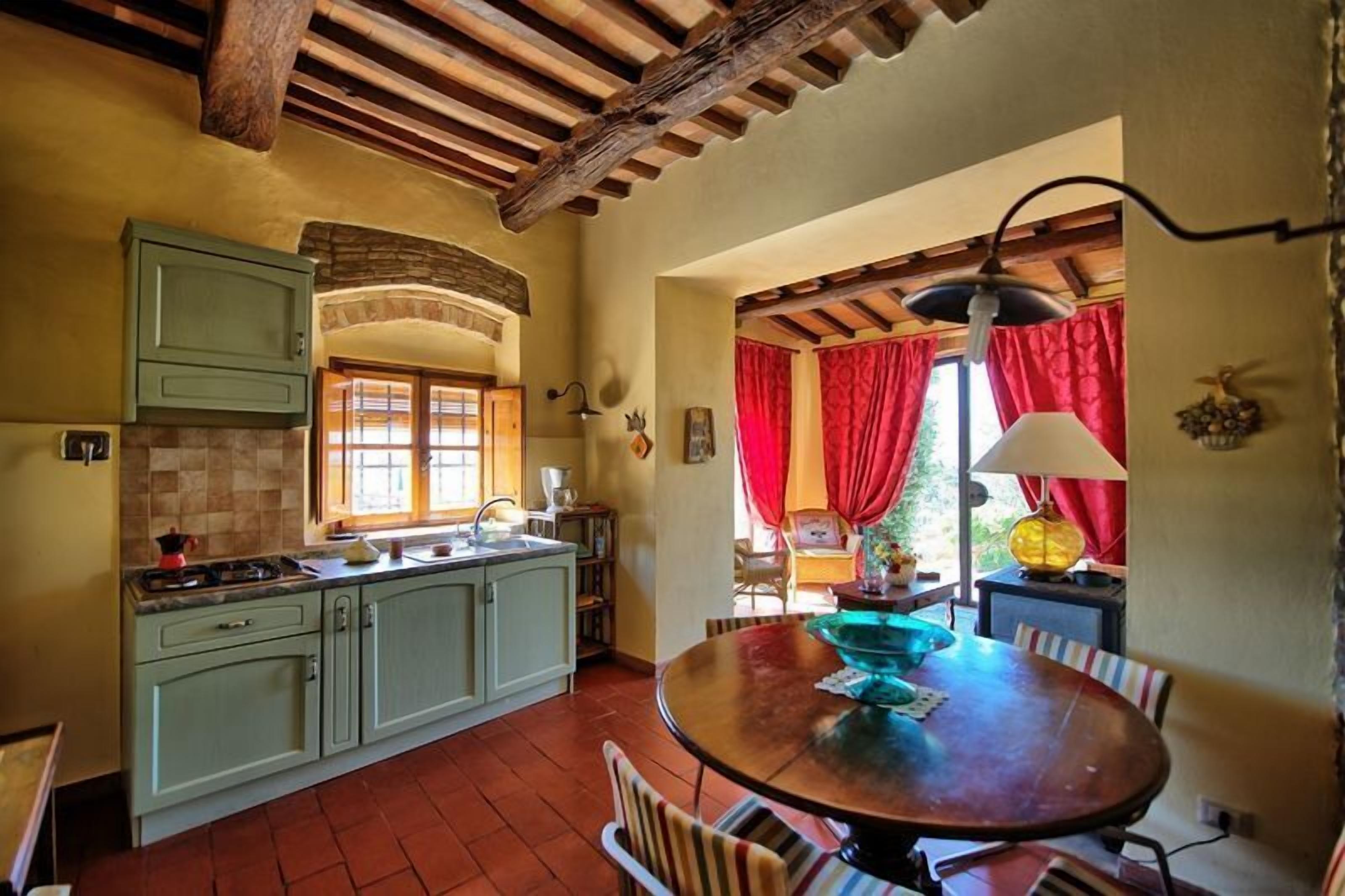 Une cuisine rustique avec un plafond en bois, une table à manger entourée de chaises et une fenêtre ornée de rideaux rouges.