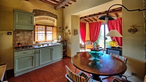 Una cuina rústica amb sostre de fusta, una taula de dinar amb cadires i una finestra amb cortines vermelles.