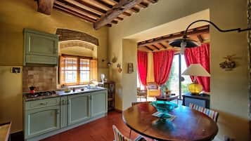Une cuisine rustique avec un plafond en bois, une table à manger entourée de chaises et une fenêtre ornée de rideaux rouges.