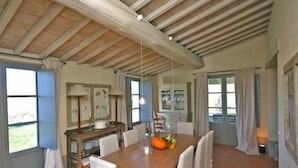 A dining area with a wooden table, white chairs, a chandelier, and a view of the outdoors. - Villa Danilo (San Casciano dei Bagni)