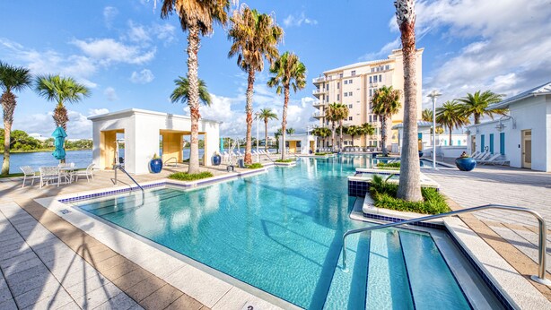 Une piscine à l’eau d’un bleu cristallin, entourée de palmiers et bordée d’un bâtiment doté de balcons.