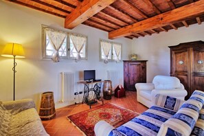 Un salon chaleureux avec un plafond en bois, un canapé, un fauteuil, une lampe, un téléviseur, un radiateur et un meuble.