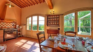 Eine Küche mit großem Fenster, Holzbalken an der Decke und einem Essbereich, der für eine Mahlzeit gedeckt ist.