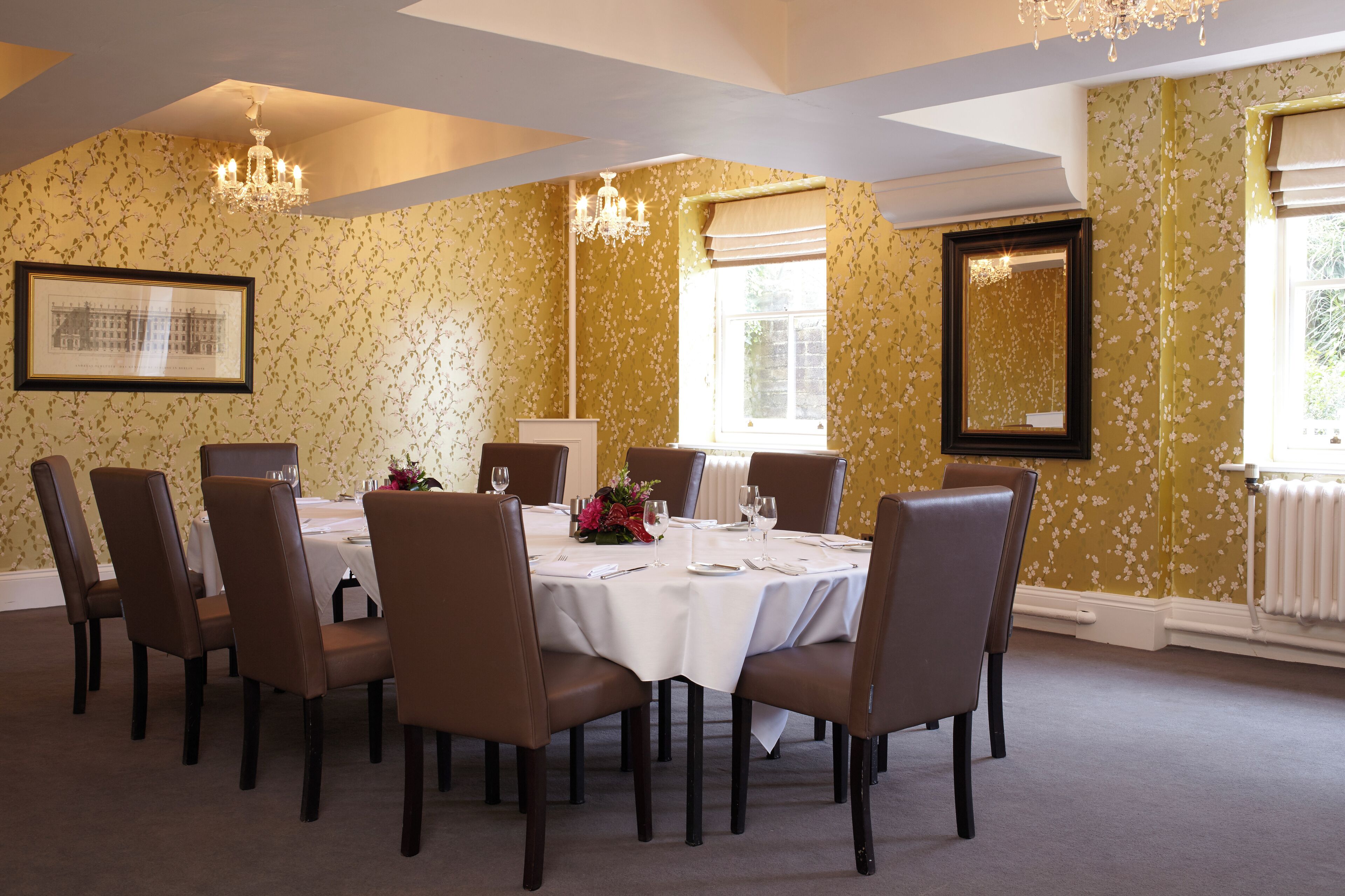 A dining room with a round table set for six, surrounded by six brown chairs.