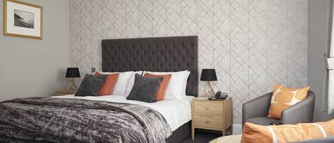 A modern bedroom with a large bed, bedside tables, a chair, and a framed picture on the wall.
