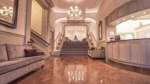 A spacious lobby with a grand staircase, a sofa, and a kitchen area. - The Royal Hotel (Ventnor)