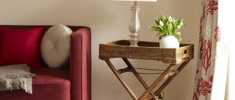 A living room with a red sofa, a white lamp, a small table with a plant, and framed artwork on the wall.