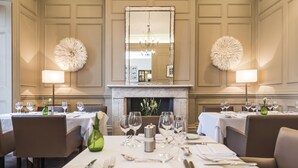 A dining area with tables set for a meal, a fireplace, and decorative wall sconces. - The Royal Hotel (Ventnor)