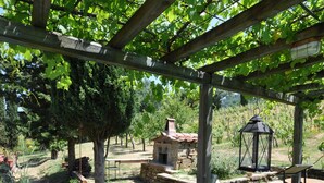 A wooden pergola with a table and chairs underneath, surrounded by greenery and a stone structure. - Villa Lo Scoiattolo (Subbiano)