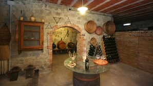 A rustic cellar with brick walls, wooden barrels, and a glass table displaying bottles and glasses. - Villa Lo Scoiattolo (Subbiano)
