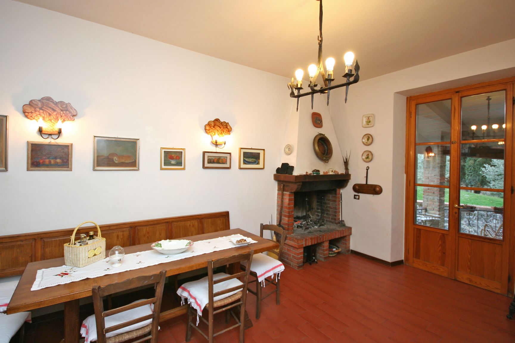 A dining area with a wooden table, chairs, a bench, a fireplace, and wall-mounted lights.