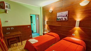Une chambre avec deux lits, un bureau et une chaise. Il y a des lampes fixées au mur et un tableau accroché au mur.