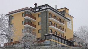Un immeuble à plusieurs étages doté de balcons, d’une façade en pierre et situé dans un environnement enneigé.
