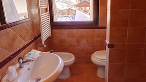 Une salle de bain avec un lavabo, deux toilettes, une fenêtre et un porte-serviettes.