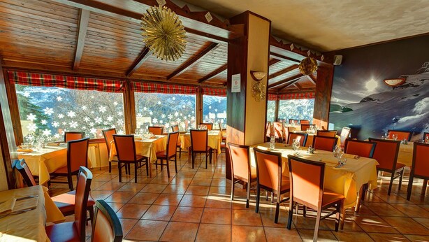 Un restaurant avec des poutres en bois au plafond, de grandes fenêtres donnant sur la verdure et des chaises et des tables de couleur orange.