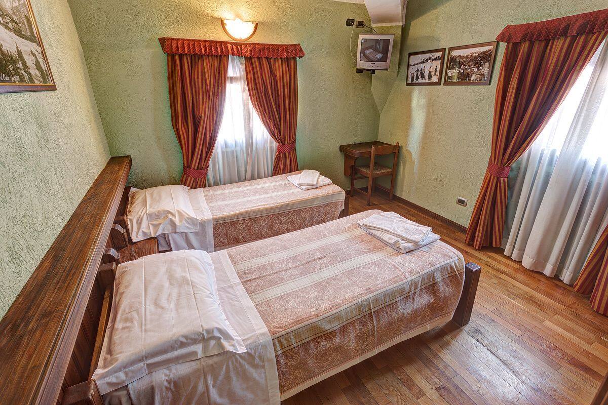 Ein Zimmer mit zwei Einzelbetten, einer hölzernen Bank, einem kleinen Tisch und einem an der Wand befestigten Fernseher.