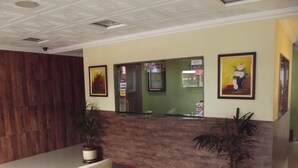 A reception area with a wooden wall, a reception desk, two potted plants, a framed painting, and a no-smoking sign. - Charlott Hotel (São Paulo)