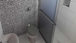 A bathroom with a patterned wall, a toilet, a sink, and a shower door. - Charlott Hotel (São Paulo)