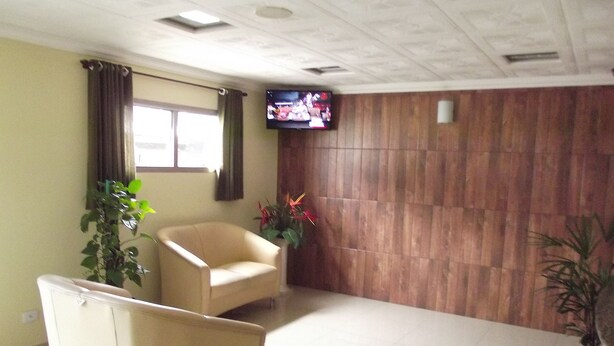 A room with a beige armchair, a television on the wall, and a wooden panel wall. - Charlott Hotel (São Paulo)