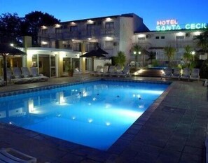 Hotel met een zwembad, ligbedden en een bord waarop 'HOTEL SANTA CECELA' staat.