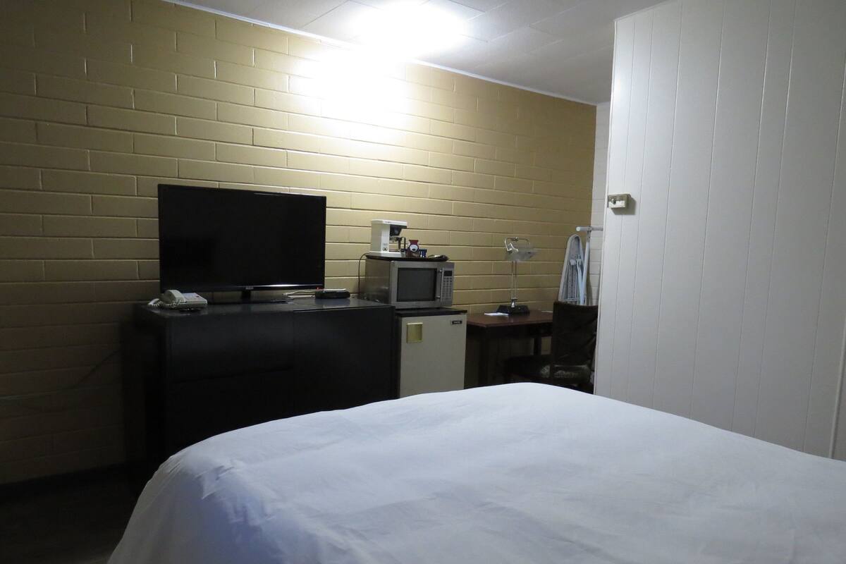 A hotel room with a bed, a TV, a microwave, a desk, and a chair.