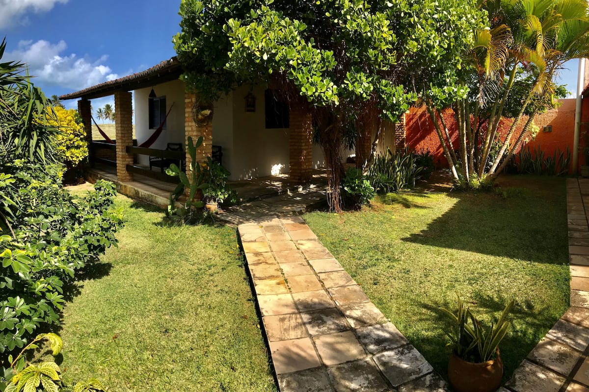 A well-maintained garden with a paved walkway leading to a house with a tiled roof and a hammock.