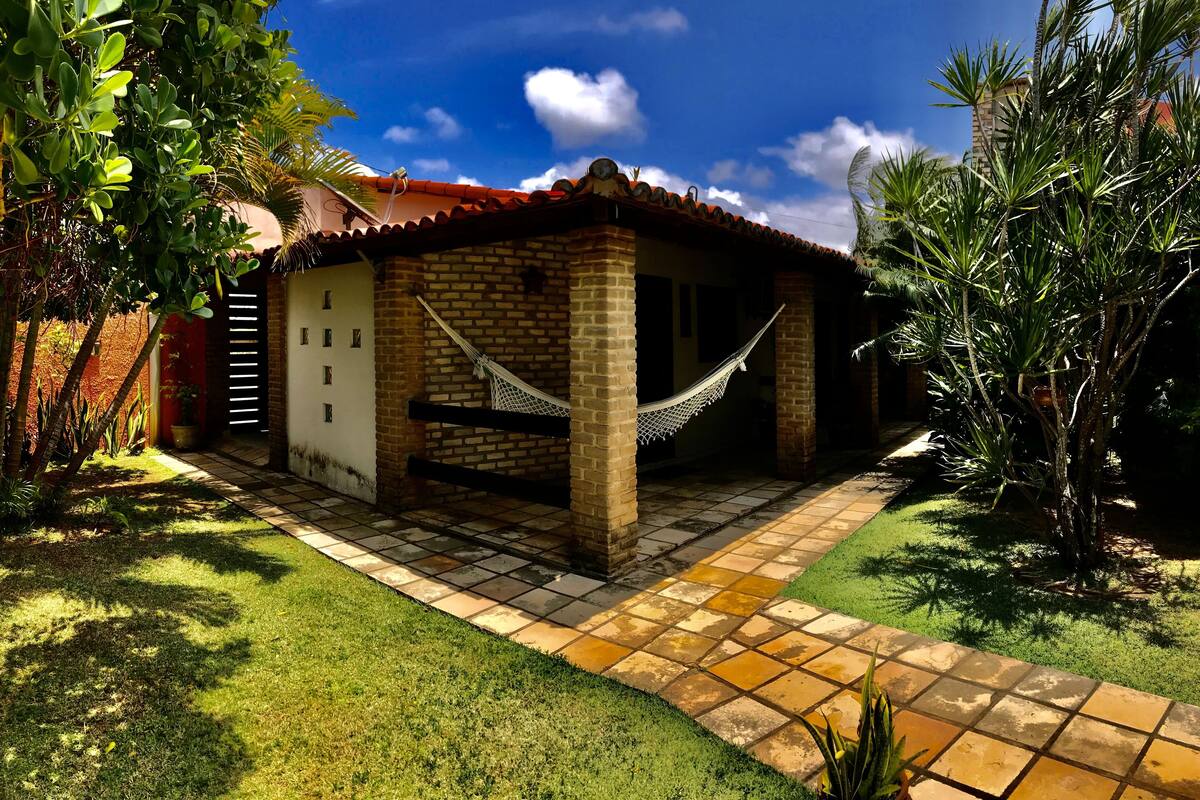 A small, single-story house with a red-tiled roof, a hammock, and a brick exterior.