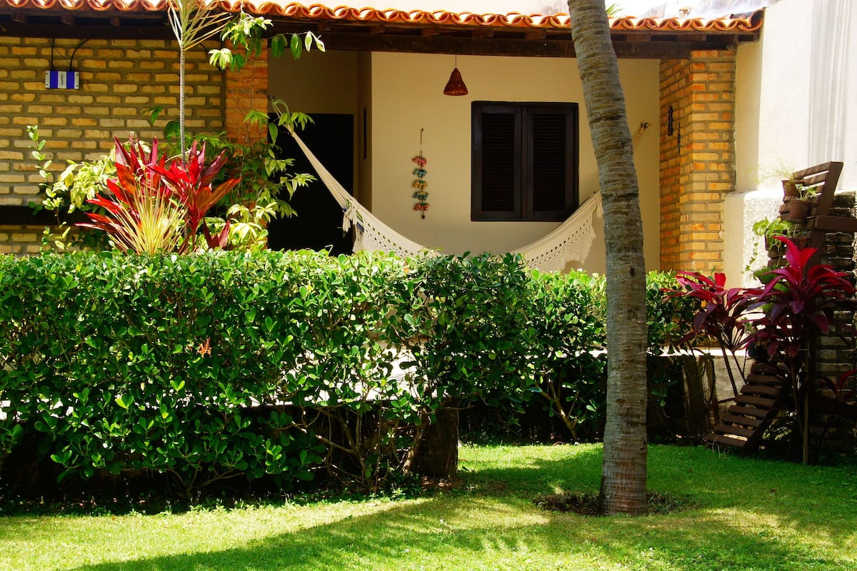 A house with a brick exterior, a hammock, and various plants in the yard.