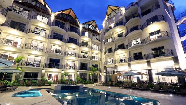 A multi-story hotel with balconies, a swimming pool, and outdoor seating areas. - Luxury Sky Penthouses 3-6BR Condo-Hotel at Oceano Jaco (Jacó)