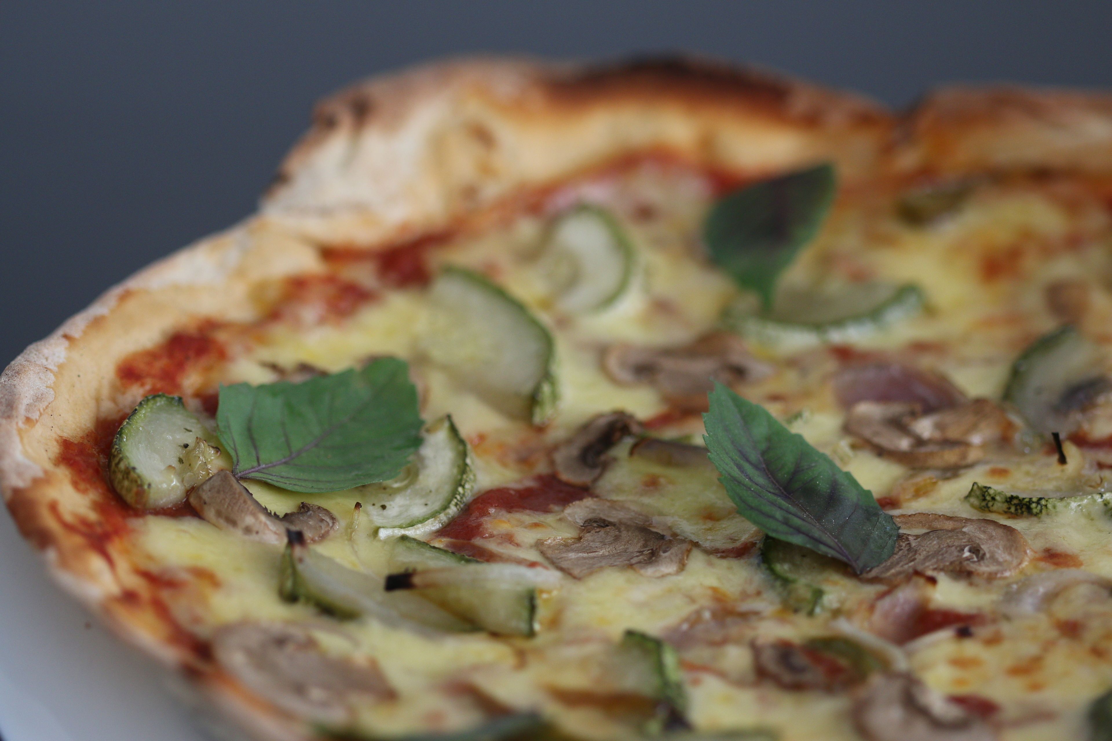 A close-up of a pizza with zucchini, mushrooms, and basil leaves.