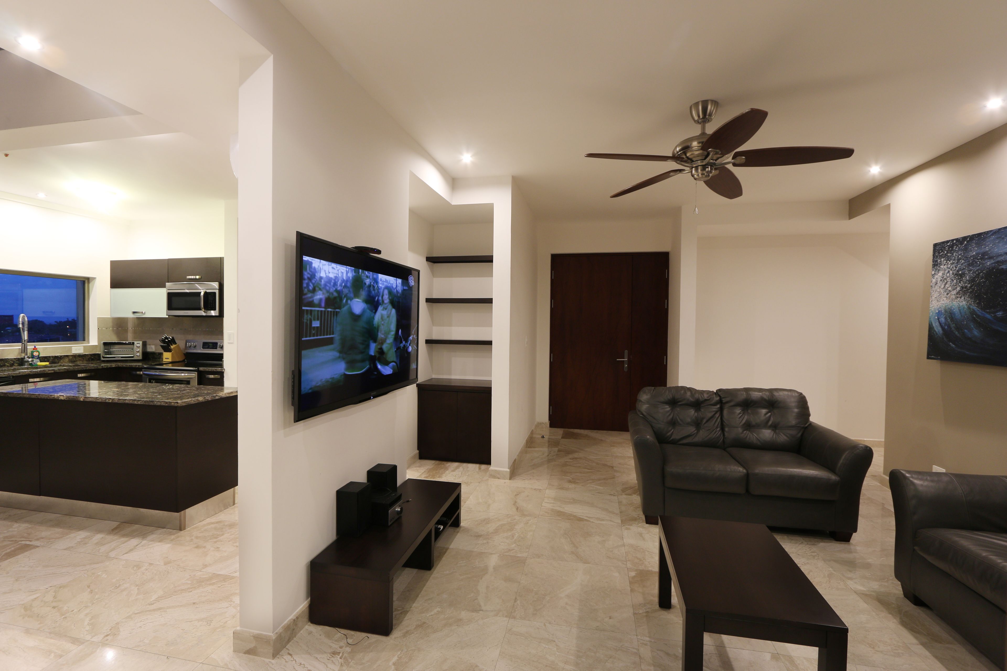 Een moderne woonkamer met een flatscreen televisie, een plafondventilator en een leren bank.