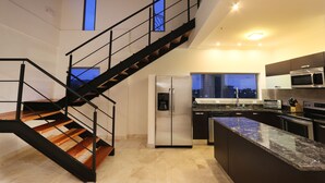 A modern kitchen with a built-in island, stainless steel appliances, and a staircase with a black railing. - Luxury Sky Penthouses 3-6BR Condo-Hotel at Oceano Jaco (Jacó)