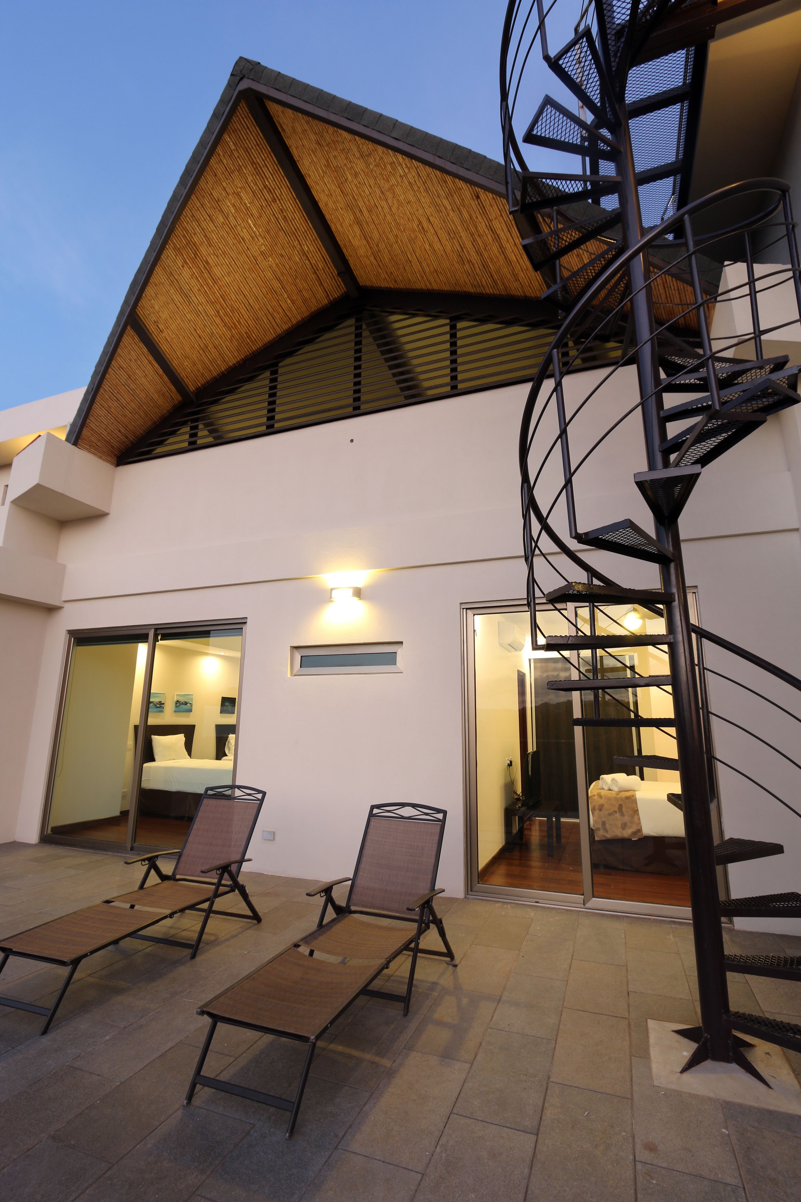 Un bâtiment moderne doté d’un escalier en colimaçon, d’un espace extérieur aménagé avec des fauteuils confortables, et d’une entrée avec une porte en verre.