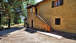 A rustic building with a stone staircase leading to a wooden door, surrounded by trees and gravel. - Vittoriana (San Gimignano)