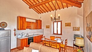 A compact kitchen with wooden cabinets, a dining area with a table and chairs, a sofa, and a chandelier. - Vittoriana (San Gimignano)