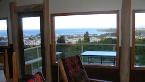 Una habitación con vistas a un pueblo costero, una silla de madera con un cojín estampado y una mesa con estructura metálica.
