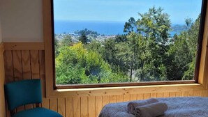 Un dormitorio con un amplio ventanal que ofrece vistas al mar y al follaje.